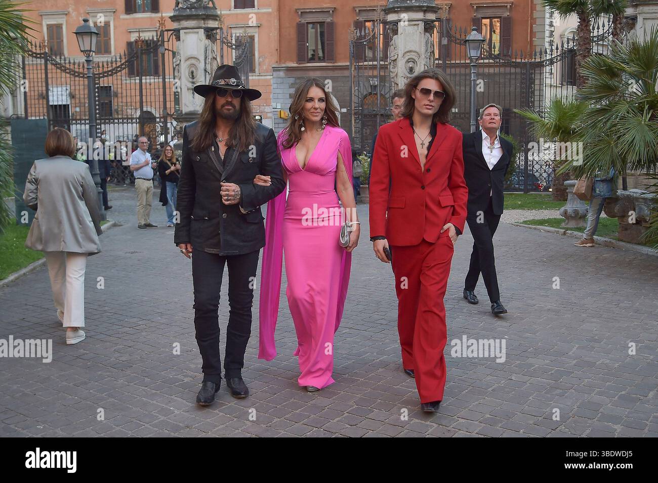 Italien, Rom, 24. Mai 2025 - Liz Hurley betäubt sich in einem rosa Outfit, als sie Hand in Hand mit ihrem Partner Billy Ray Cyrus auf ihrem ersten Gesellschaftsausflug zusammen mit Liz' Sohn Damian Charles Hurley auf dem roten Teppich zur Eröffnung der Orizzonti/Rosso-Ausstellung von Valentino Garavani und Giancarlo Giammetti in Rom geht. Foto © Fabio Mazzarella/Sintesi/Alamy Live News Stockfoto