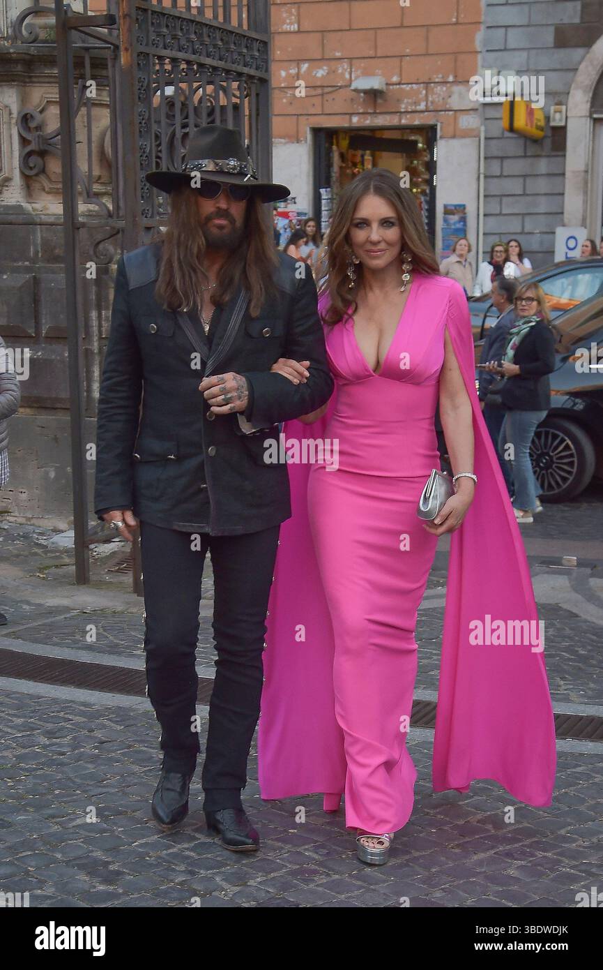 Italien, Rom, 24. Mai 2025 - Liz Hurley betäubt sich in einem rosa Outfit, als sie Hand in Hand mit ihrem Partner Billy Ray Cyrus auf ihrem ersten Gesellschaftsausflug zusammen mit Liz' Sohn Damian Charles Hurley auf dem roten Teppich zur Eröffnung der Orizzonti/Rosso-Ausstellung von Valentino Garavani und Giancarlo Giammetti in Rom geht. Foto © Fabio Mazzarella/Sintesi/Alamy Live News Stockfoto