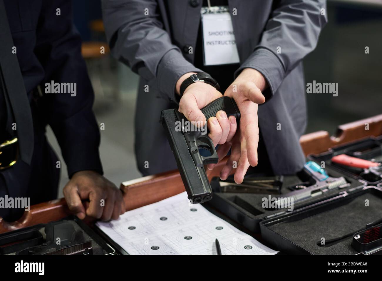 Nahaufnahme, in der der Kursleiter die Person während der Sicherheitsschulung für Schusswaffen in einer Umgebung mit Innenbereich in der richtigen Handhabung von Handfeuerwaffen führt Stockfoto