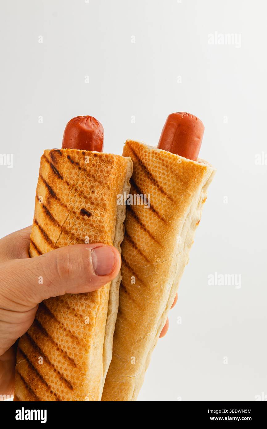 Eine Person hält zwei gegrillte Hot Dogs in gerösteten Brötchen. Die Szene hebt die köstliche Textur und Farbe des Essens hervor, geeignet für legere din Stockfoto