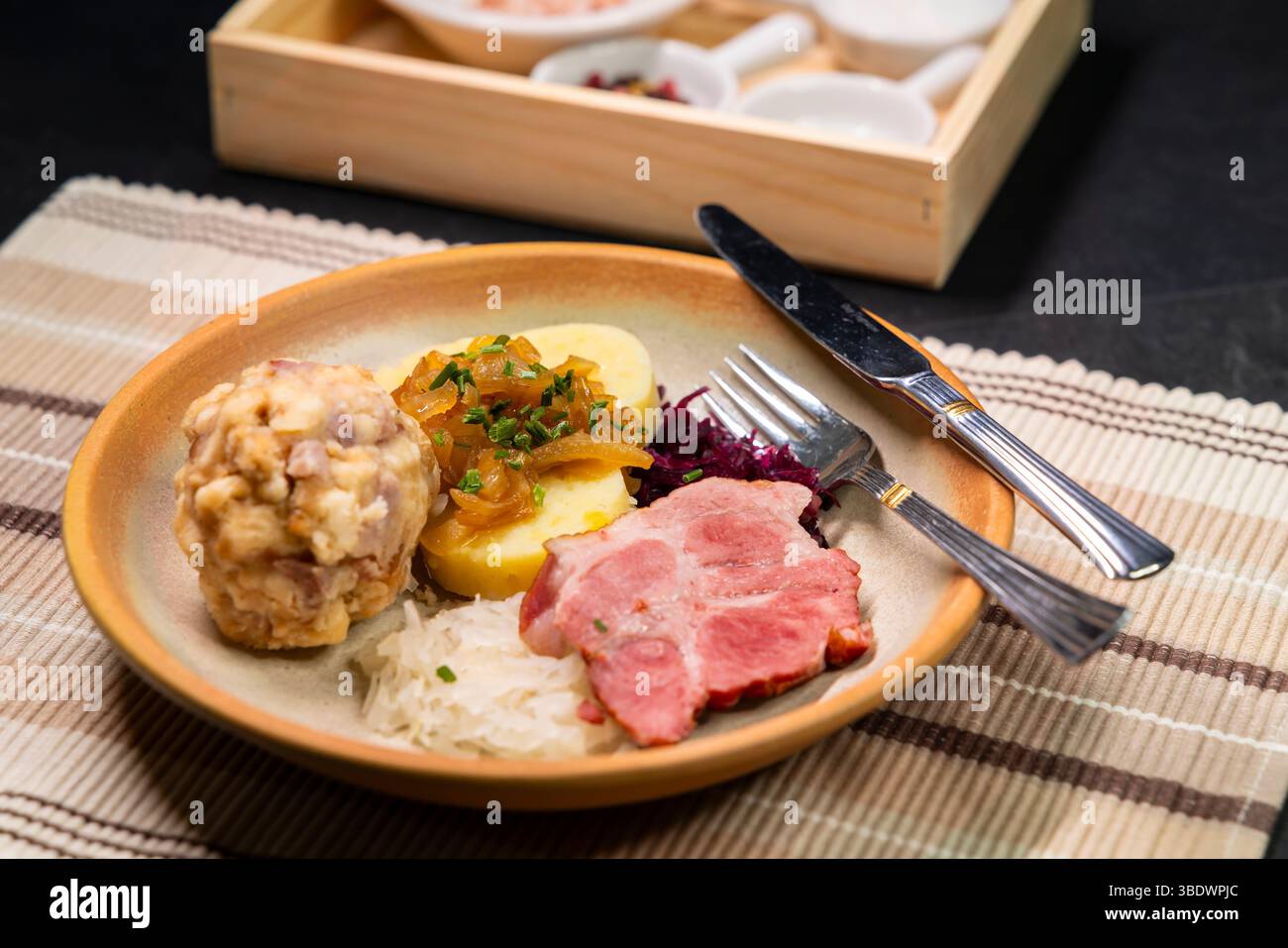 Deftige bayerische Spezialitäten mit Knödeln, gebratenem Schweinefleisch, Sauerkraut und karamelisierten Zwiebeln als Nahaufnahme auf einem Teller Stockfoto