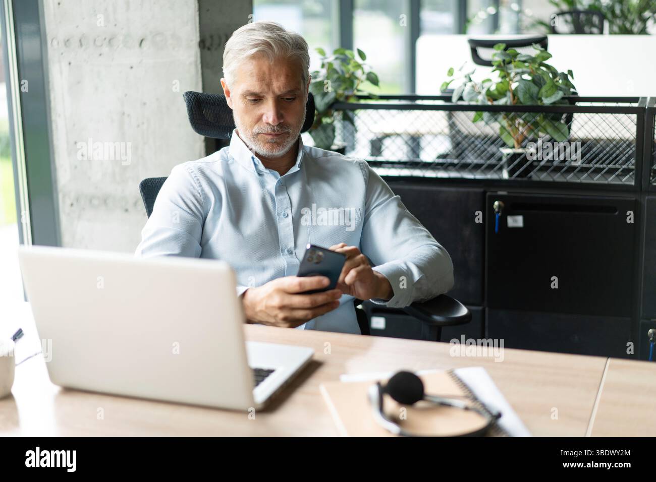 Geschäftsmann mittleren Alters, der ein Smartphone hält. Reifer 45-jähriger Geschäftsmann, Geschäftsinhaber oder Unternehmer, der am Schreibtisch sitzt und mit m Stockfoto