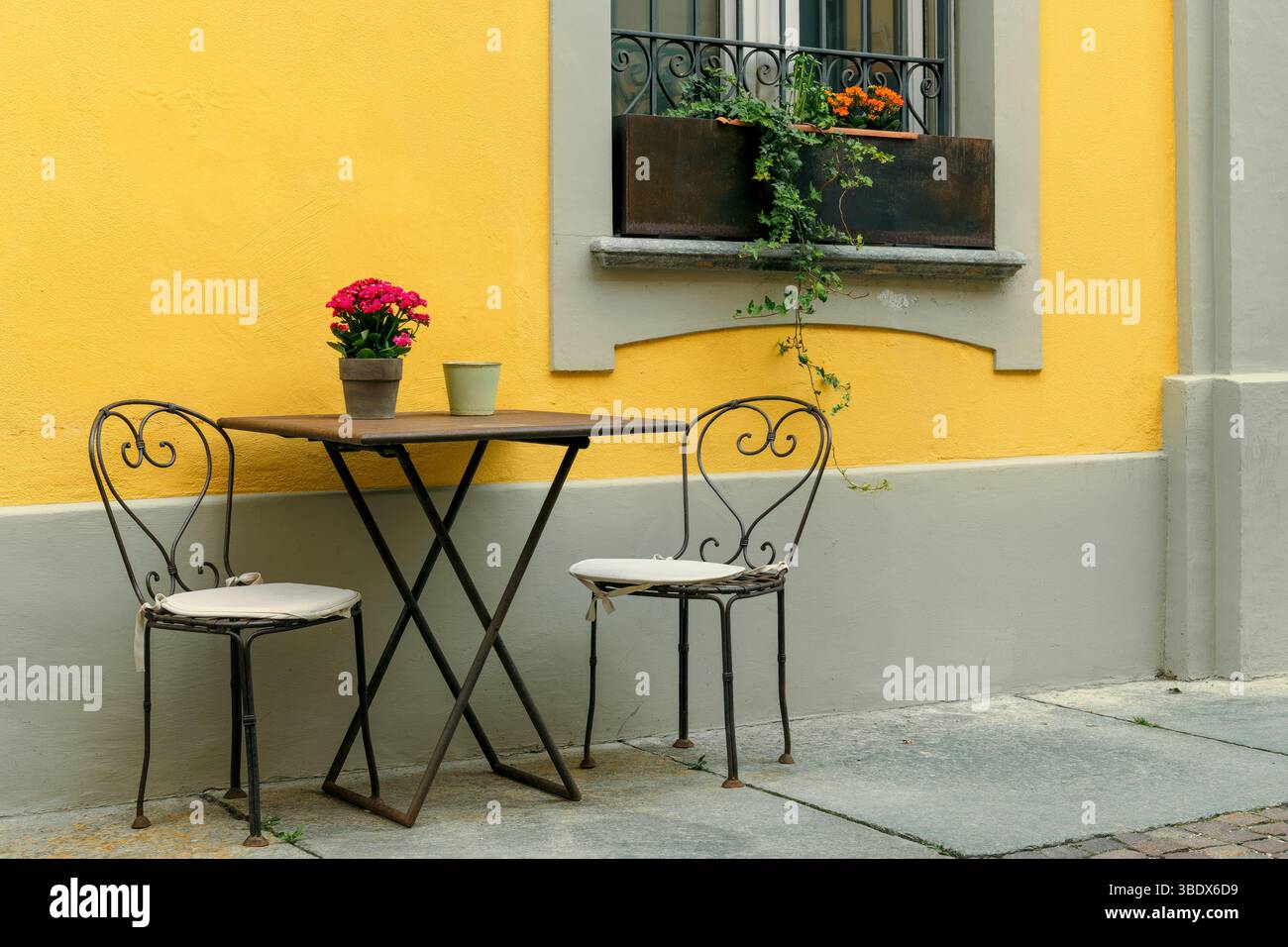 In einem Restaurant im Freien in der Altstadt von Alba, Italien, stehen Stühle und ein Tisch an der gelben Wand. Stockfoto