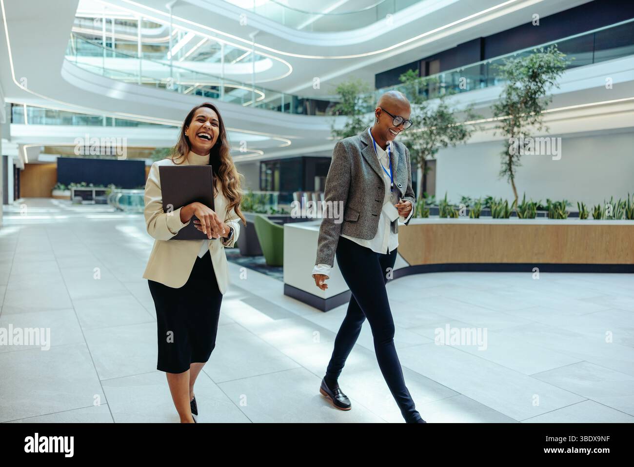 Zwei Profis, ein indischer und ein afrikanischer, laufen durch ein modernes Büro, lachen und genießen Gespräche. Die Umgebung ist hell und beschaulich Stockfoto