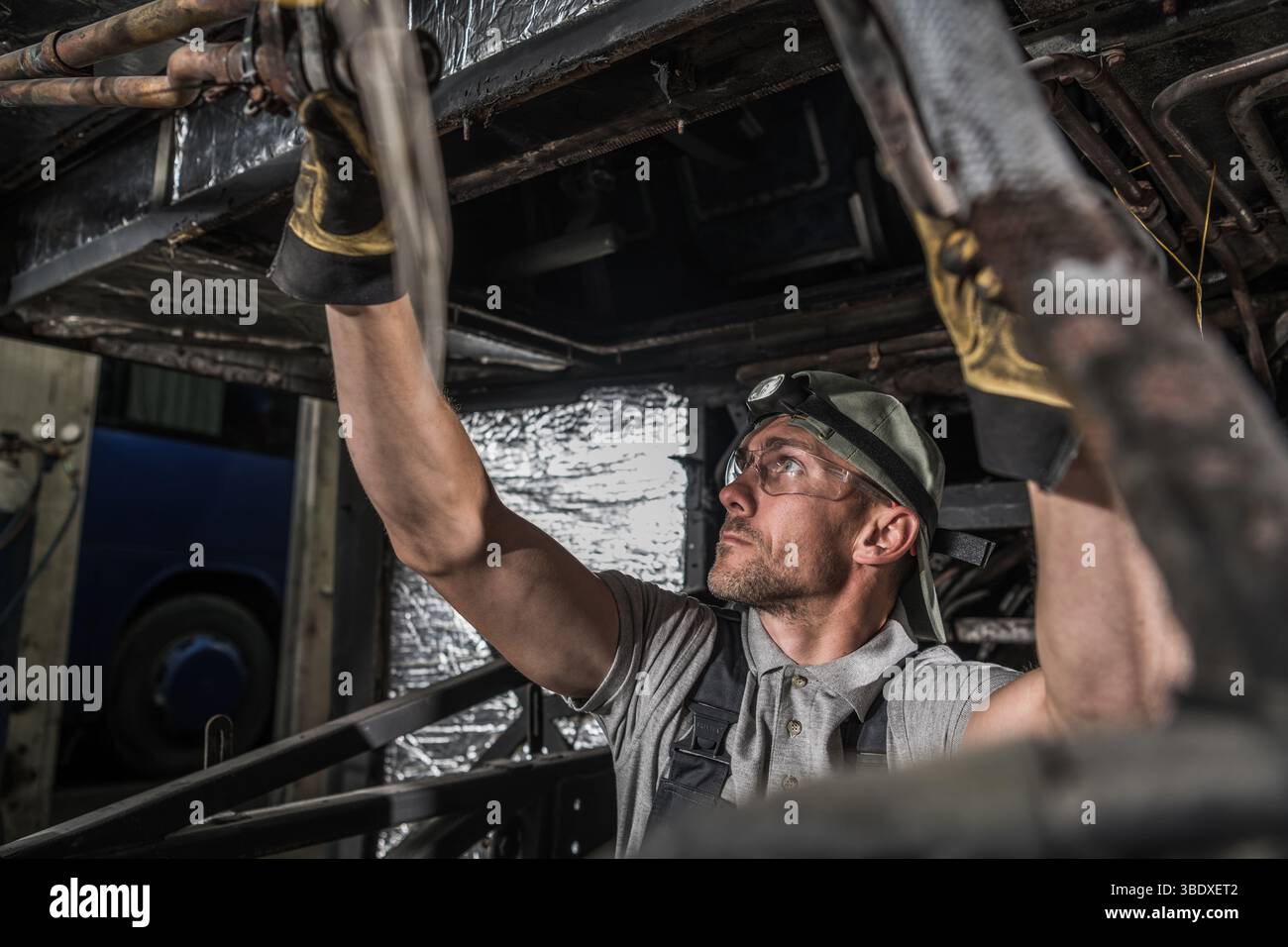 Ein Mechaniker inspiziert die Unterseite eines Fahrzeugs in einer Werkstatt, stellt die Werkzeuge ein und konzentriert sich auf die anstehende Aufgabe. Stockfoto