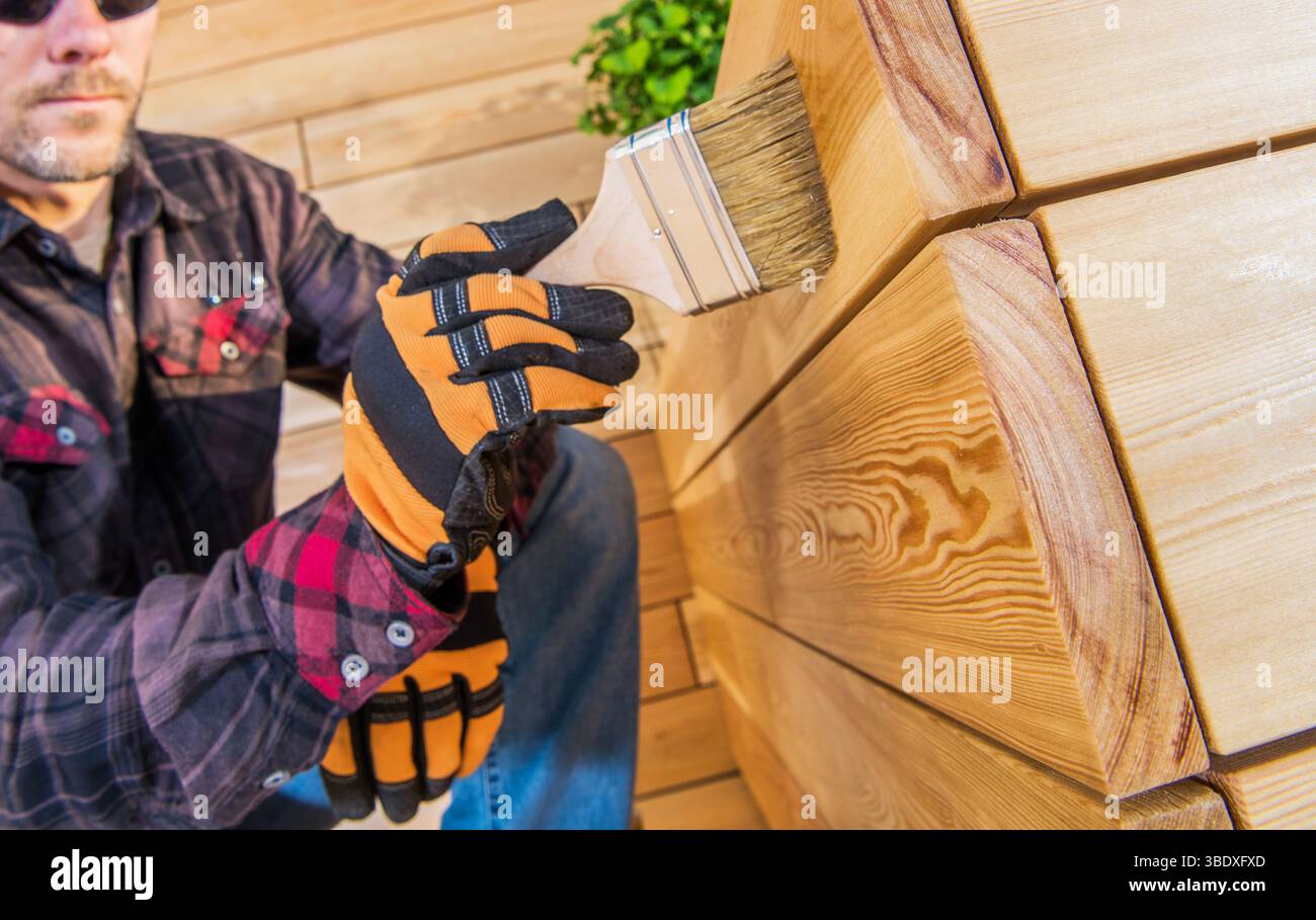 Eine Person malt sorgfältig mit einem Pinsel eine Holzoberfläche und zeigt bei einer Heimwerkeraufgabe Liebe zum Detail. Weiches natürliches Licht sorgt für Wärme im Stockfoto