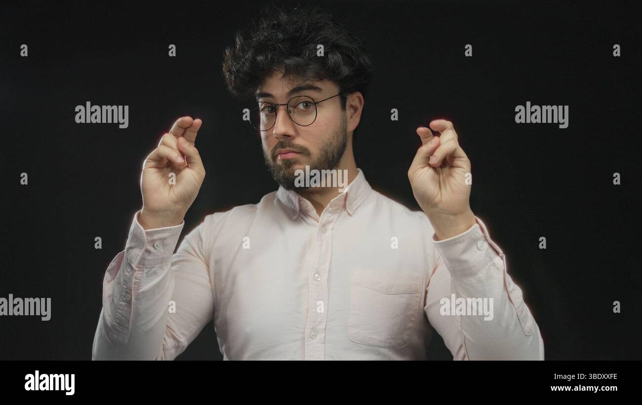 Junger Mann mit Bart und Brille, der vor schwarzem Hintergrund eine Geste angibt, die Ausdruck und Geste in einem Studio zeigt. Stockfoto