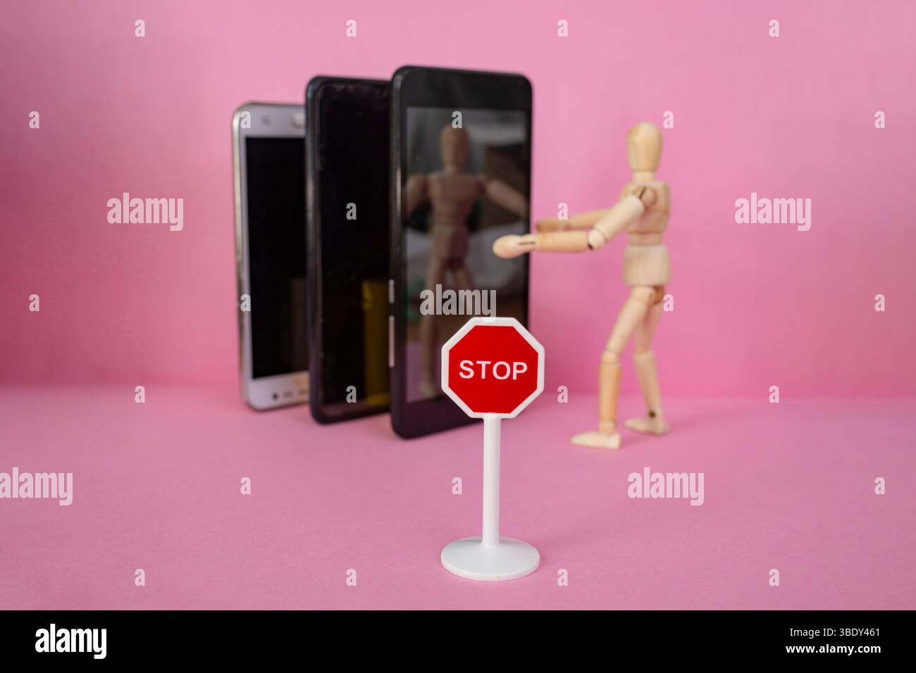 Hölzerne Schaufensterpuppe, die Smartphones auf rosa Hintergrund umschließt, ein Selfie macht, mit einem Stoppschild, Miniatur Stockfoto