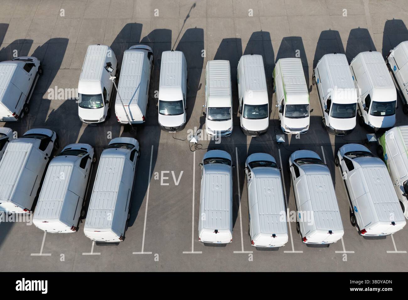 Reihen von weißen Elektro-Lieferwagen an Ladestationen für Elektrofahrzeuge. Stockfoto