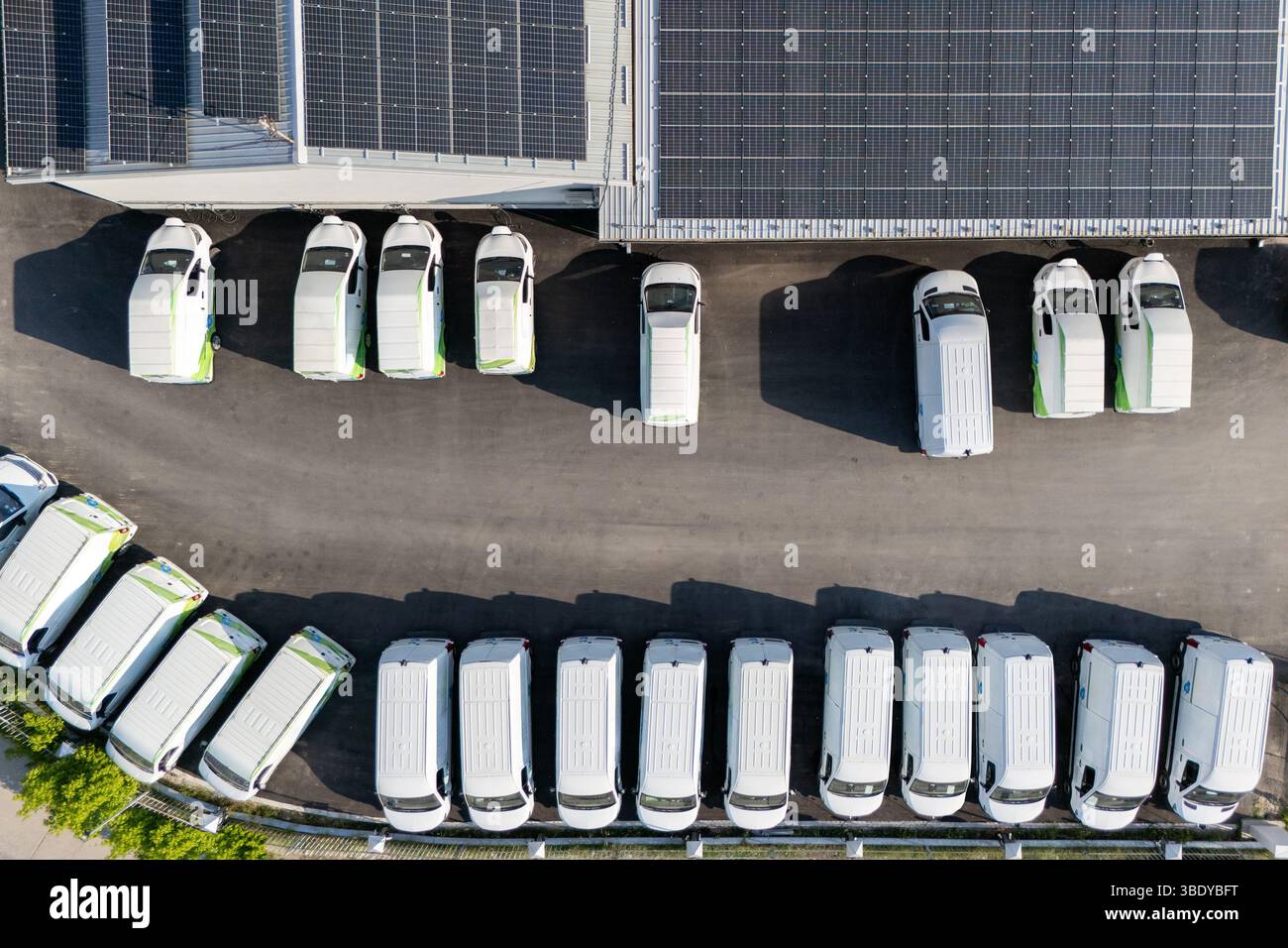 Reihen von weißen Elektro-Lieferwagen an Ladestationen für Elektrofahrzeuge. Stockfoto