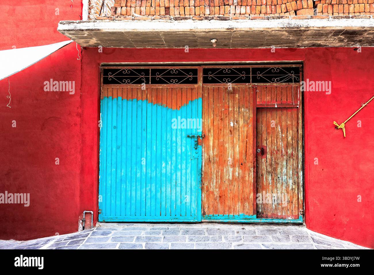 Atontonilco, Mexiko - 29. Mai 2016: Ein pulsierendes rotes Gebäude mit teilweise blau-orange lackierter Tür, die den farbenfrohen Architekten der Stadt zeigt Stockfoto