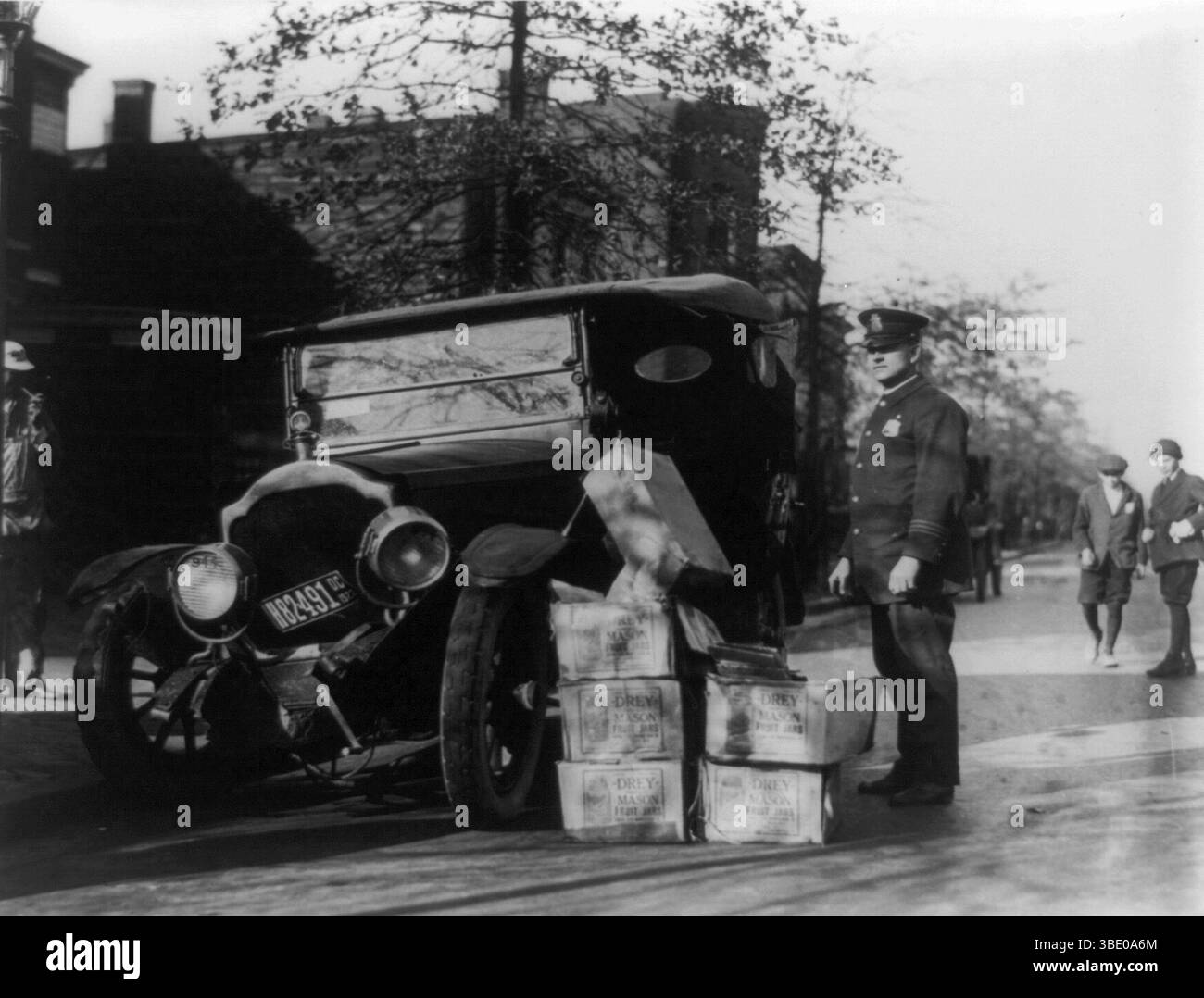 Ein Polizist mit kaputtem Auto und konfisziertem Mondschein, 1922. Zwischen 1920 und 1933 war der Verkauf und die Destillierung von Alkohol in den USA verboten. Dies führte dazu, dass die illegale Produktion zu einem massiven Industriezweig wurde, und Autounfälle bei Polizeijagden waren keine Seltenheit. Stockfoto