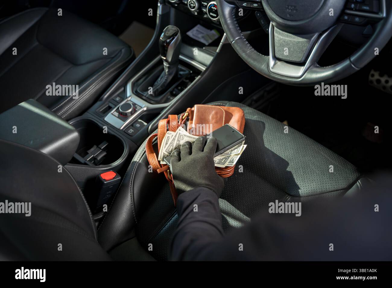 Nahaufnahme einer Hand mit Handschuhen, die Geld und ein Smartphone aus einer Ledertasche auf einem Autositz stiehlt. Konzept von Diebstahl, Raub, Fahrzeugeinbruch, Verbrechensverhütung Stockfoto