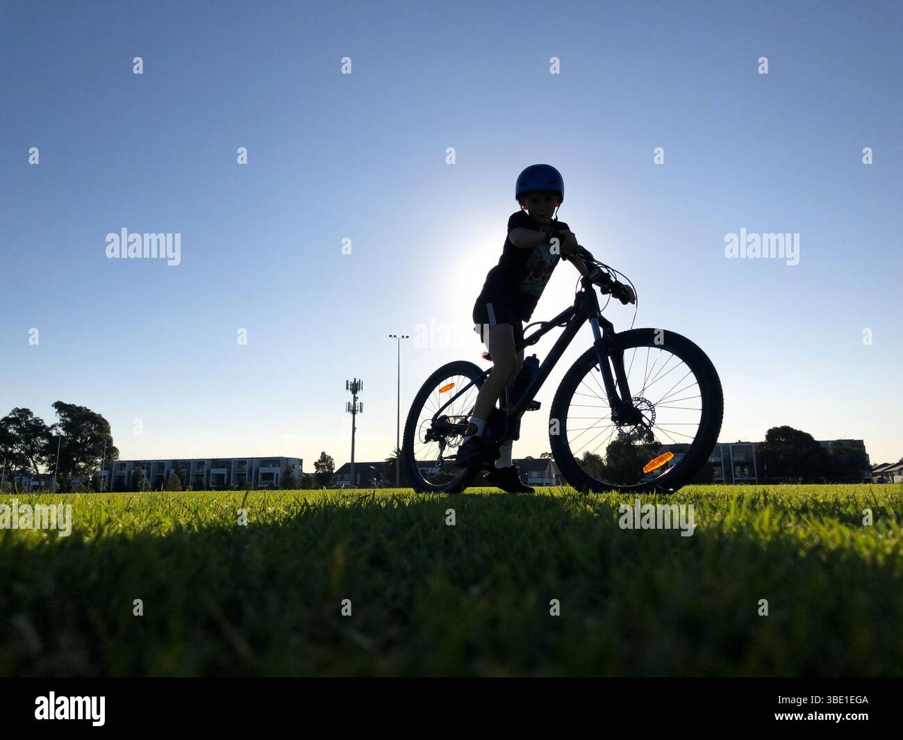 Silhouette eines Kindes, das bei Sonnenuntergang über dem Mountainbike auf dem Grasfeld steht und den Outdoor-Lifestyle im Sommer genießt Stockfoto