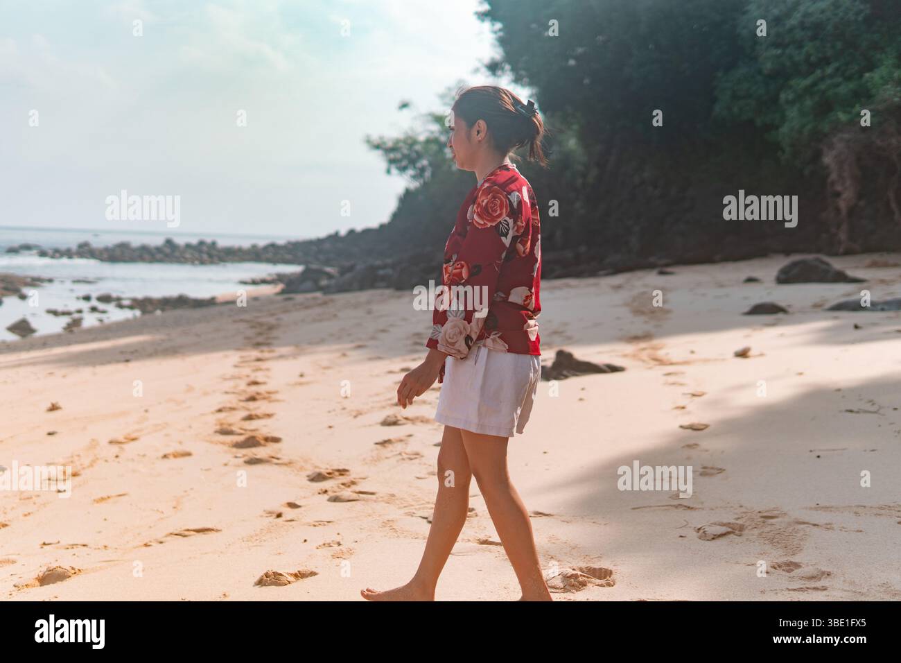 Eine indonesische Frau geht barfuß an einem ruhigen tropischen Strand und hinterlässt Spuren im Sand. Stockfoto