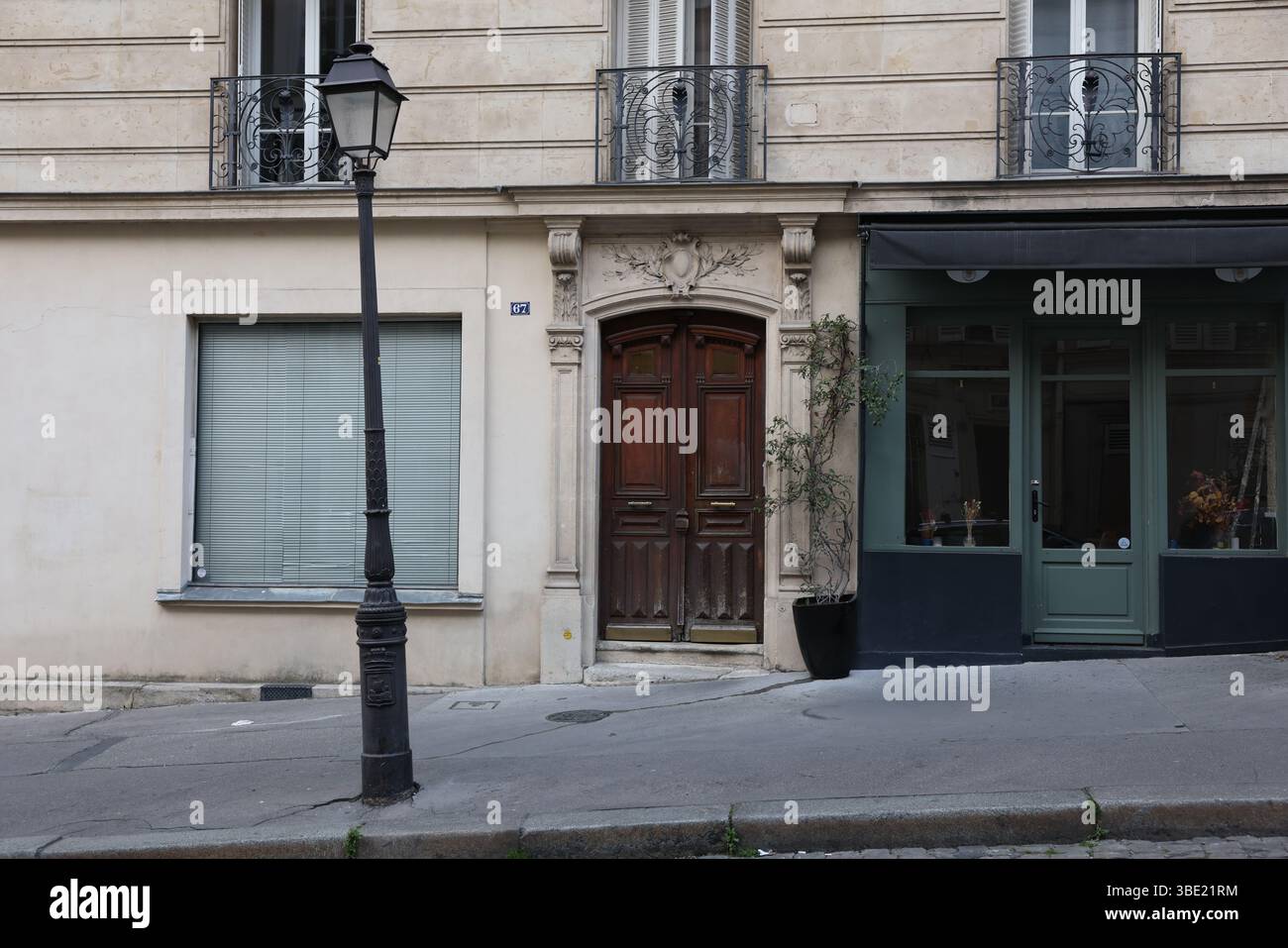 Ein detaillierter Blick auf eine Pariser Straße mit einem klassischen schwarzen Laternenpfahl. Der Schwerpunkt liegt auf einer kunstvollen Holzdoppeltür (Nummer 67) eines historischen Gebäudes Stockfoto