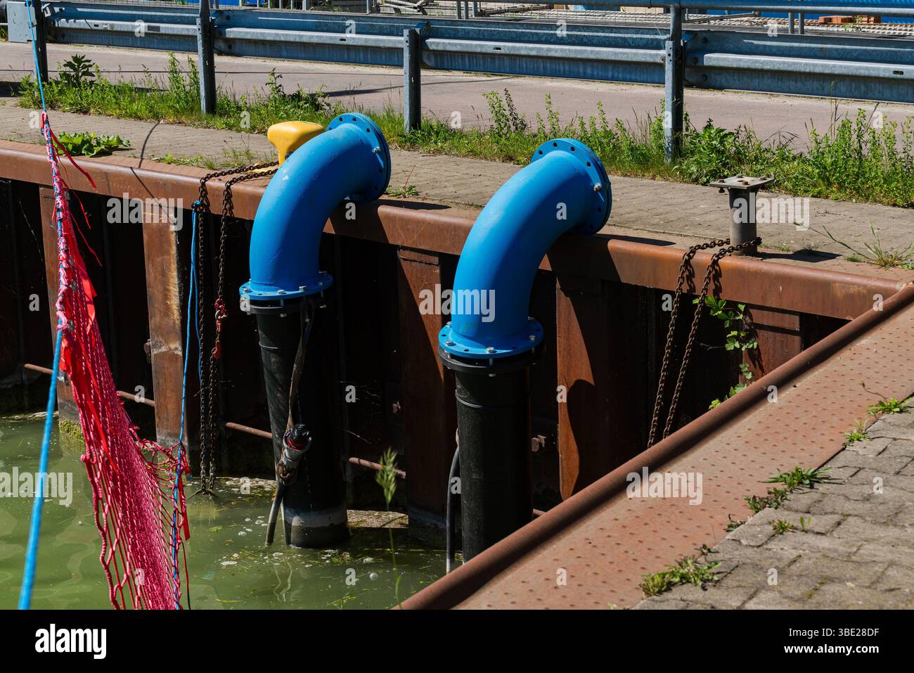 Zwei große blaue Rohre erstrecken sich von einem Dock in trübes Wasser, was auf eine industrielle Einrichtung hindeutet. Das umliegende Grün weist auf ein Gebiet hin, in dem die Natur aufeinander trifft Stockfoto