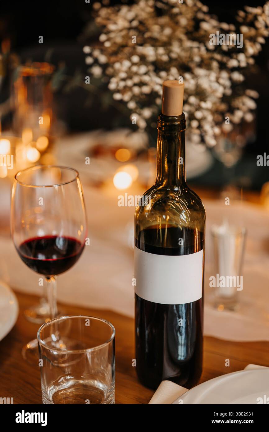 Vertikales Foto mit einem Weinglas, im Hintergrund sehen Sie eine schöne Tischdekoration. Eine Flasche Wein liegt auf einem Restauranttisch. Stockfoto