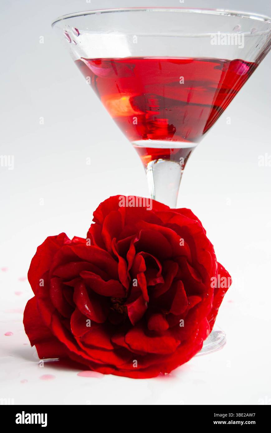 Hausgemachter Rosensirup, serviert in einem dekorativen Glas neben einer frischen Rose. Stockfoto