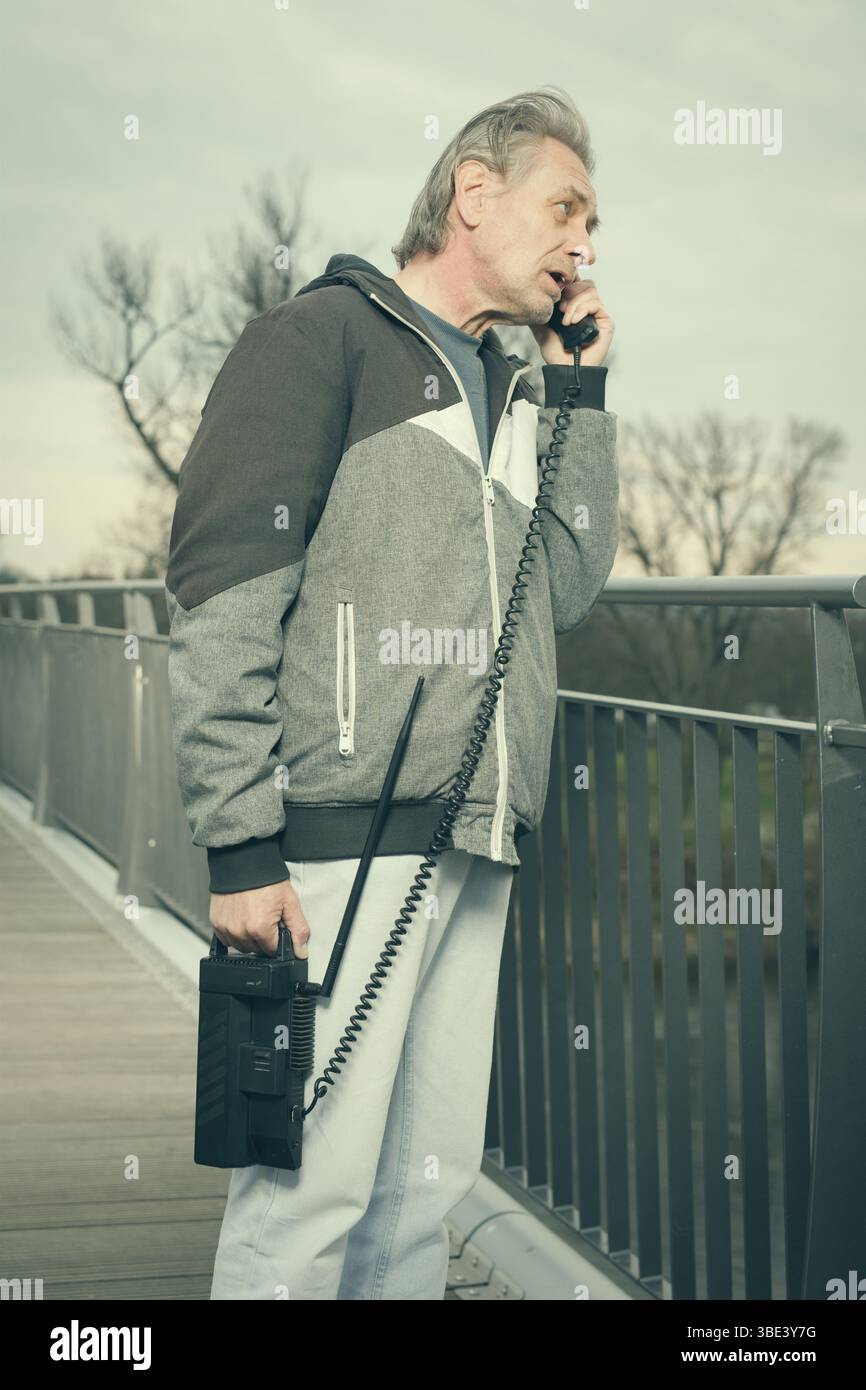 Älterer Mann draußen auf der Brücke, der ein Retro-Handy benutzt, um anzurufen Stockfoto