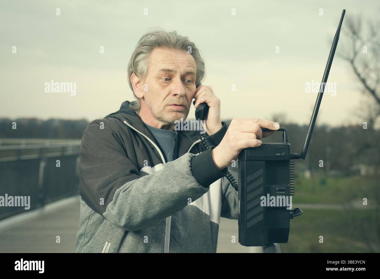Älterer Mann draußen auf der Brücke, der ein Retro-Handy benutzt, um anzurufen Stockfoto