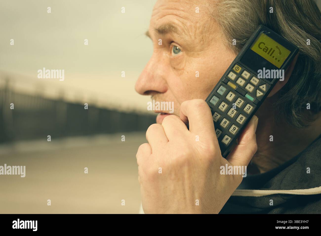Älterer Mann draußen auf der Brücke, der ein Retro-Handy benutzt, um anzurufen Stockfoto