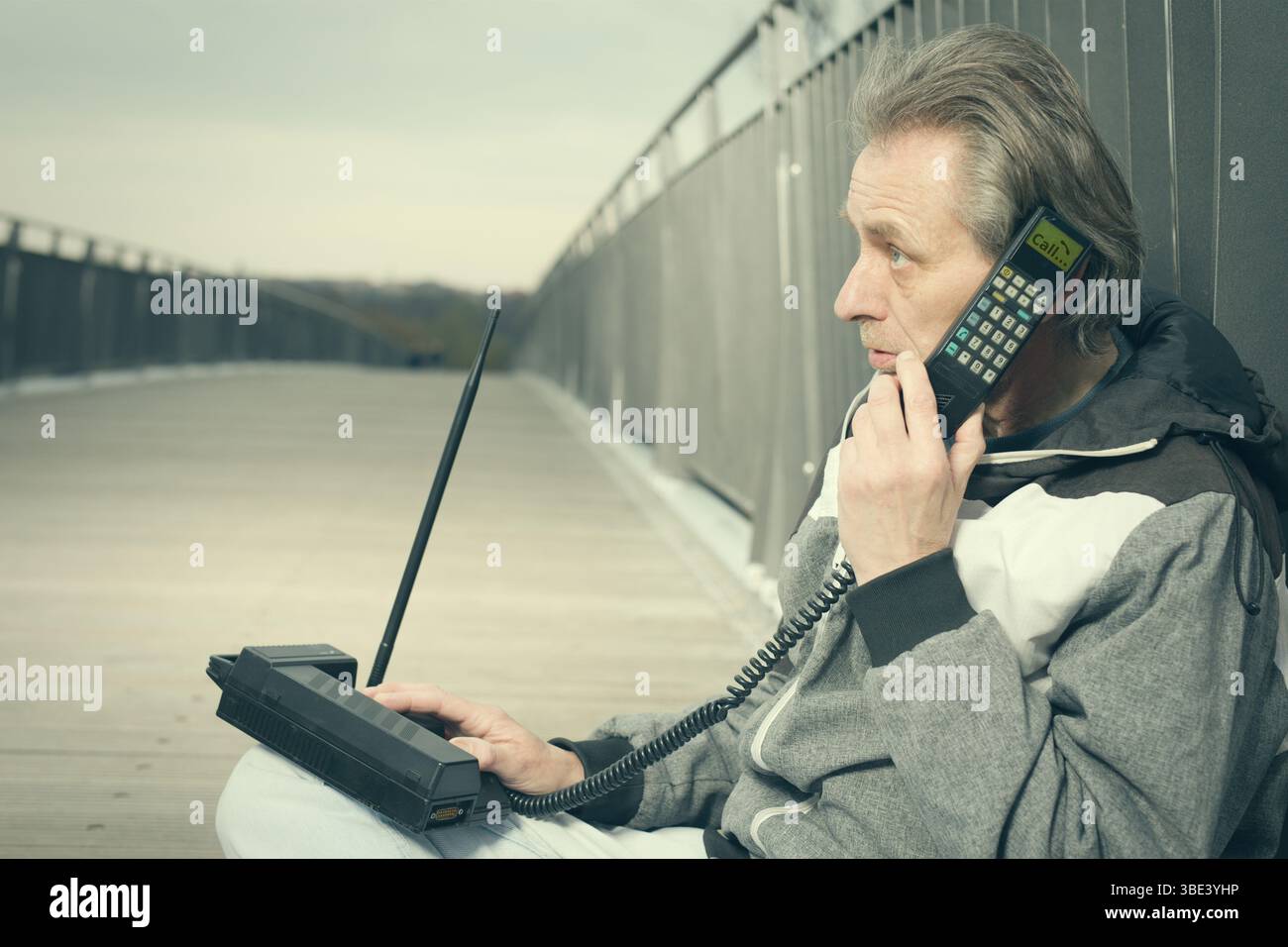 Älterer Mann draußen auf der Brücke, der ein Retro-Handy benutzt, um anzurufen Stockfoto