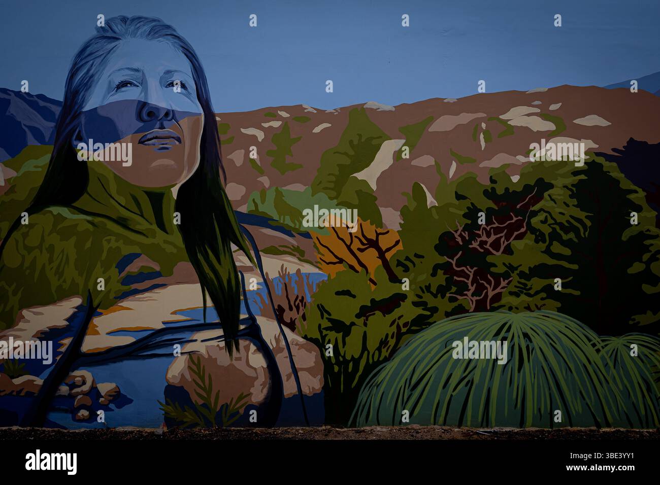 Downtown Riverside Wall Wandgemälde einer Ureinwohner, die Sie mit einer wunderschönen Landschaft im Hintergrund ansieht. Stockfoto