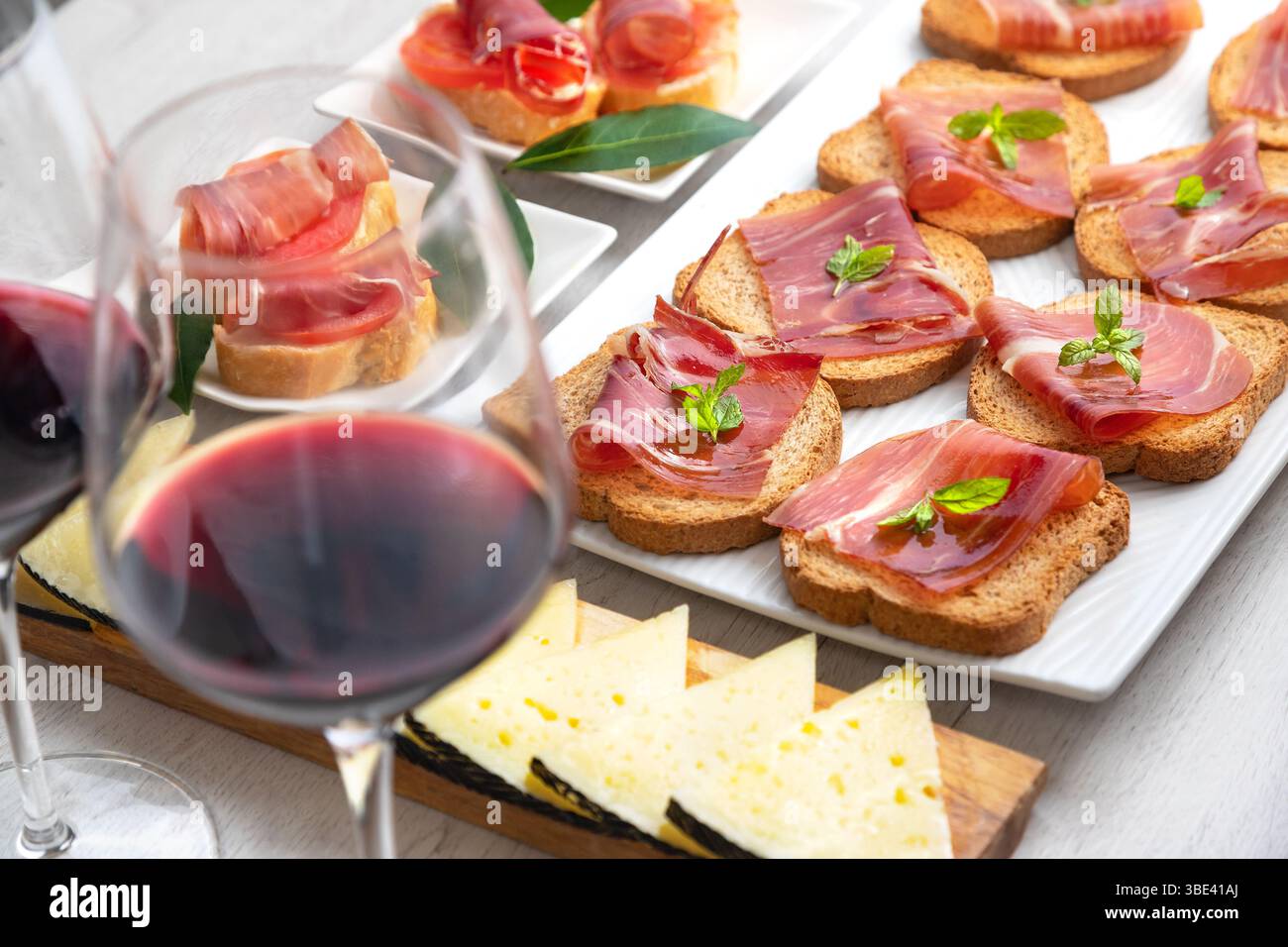 Tapas und Vorspeisen mit iberischem Schinken mit einem Glas Wein, Reifen Tomaten und Kuhkäse auf weißem Holzhintergrund. Spanische Tapas und Vorspeisen Stockfoto