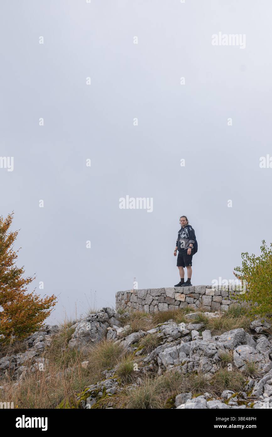 Man steht selbstbewusst auf einer runden Steinplattform mit Blick auf den nebeligen Bergwald im Herbst. Stockfoto