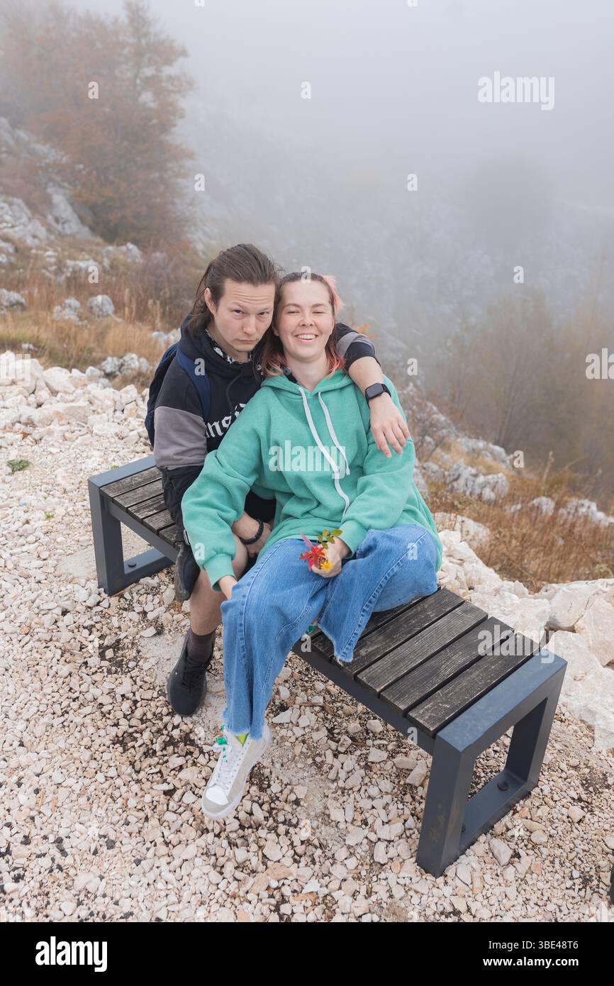 Ein Paar sitzt auf einer Bank über dem felsigen Tal, das im Morgennebel bedeckt ist Stockfoto