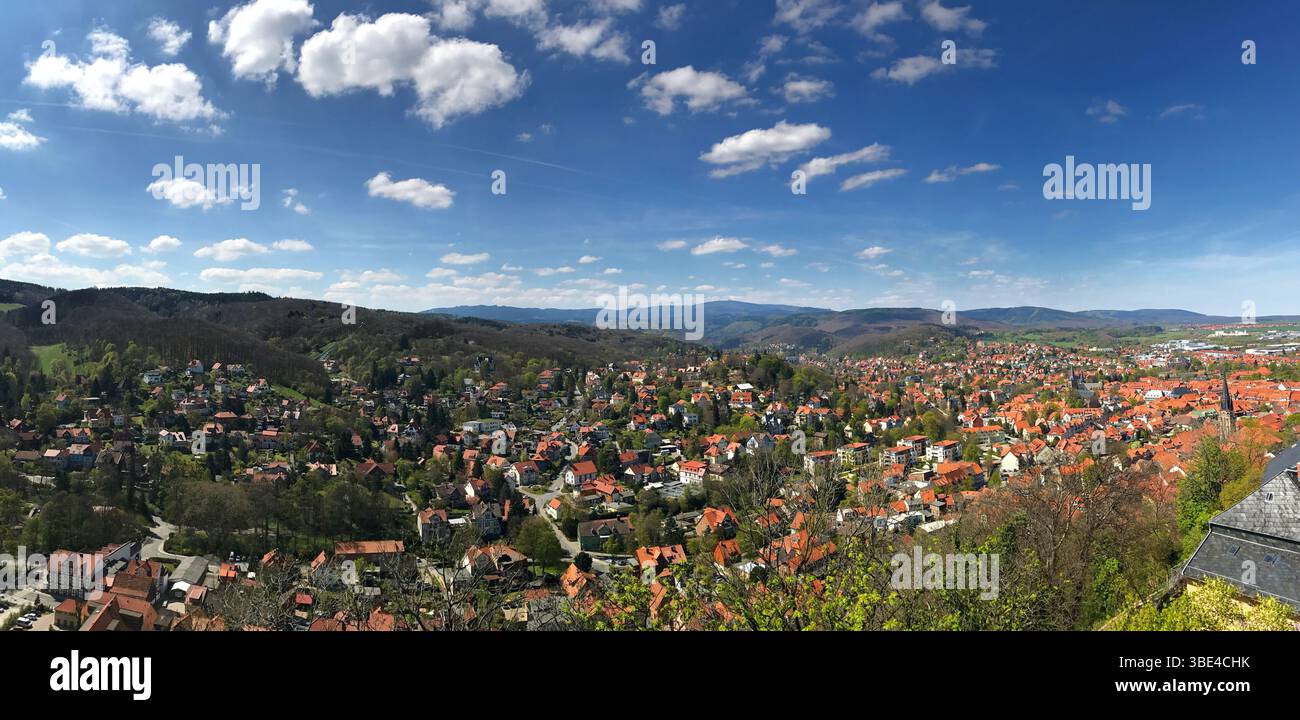 Ein breites Panorama, das eine malerische Stadt inmitten lebendiger Hügel unter einem sonnigen Himmel erfasst. Diese Hochwinkelszene zeigt üppiges Laub, rote Dächer, A Stockfoto