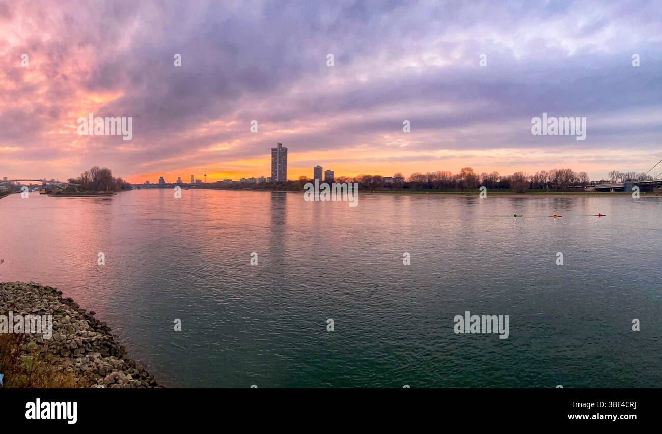 Ein friedlicher Sonnenuntergang mit einem breiten Fluss, Stadtgebäuden und farbenfrohen Kajakfahrern. Stockfoto