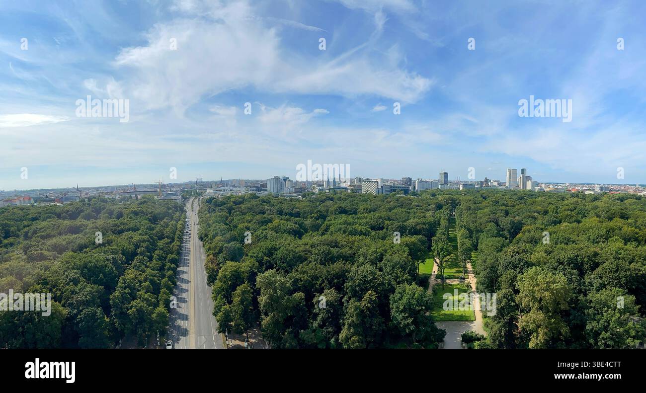 Malerisches Weitwinkelpanorama mit einer weitläufigen Skyline der Stadt, umgeben von einem weitläufigen grünen Park mit einer Straße, die unter einem leuchtenden Blau durchquert Stockfoto