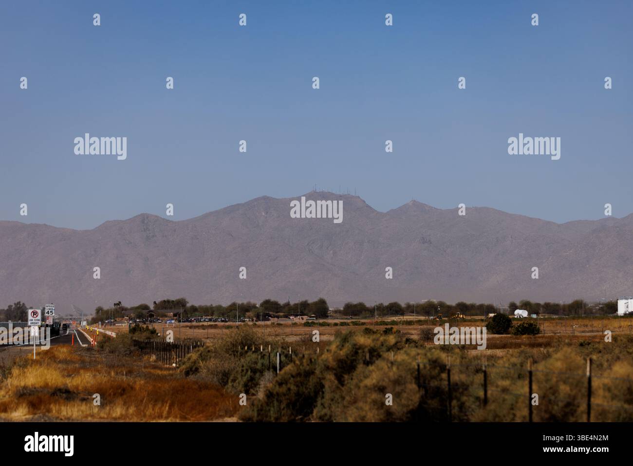 Blick auf eine ländliche Wüstenautobahn, die sich durch trockene Ebenen mit fernem Bergpanorama unter einem klaren blauen Himmel im amerikanischen Südwesten zieht. Stockfoto