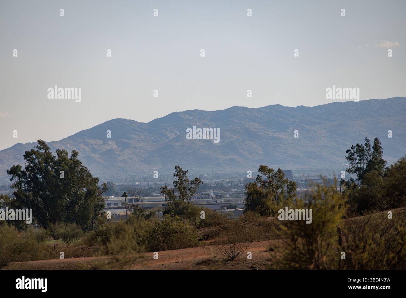 Fernblick auf eine Bergkette, die sich hinter einer vorstädtischen Wüstenlandschaft in Arizona erhebt, mit karger Vegetation unter einem klaren blauen Himmel. Stockfoto