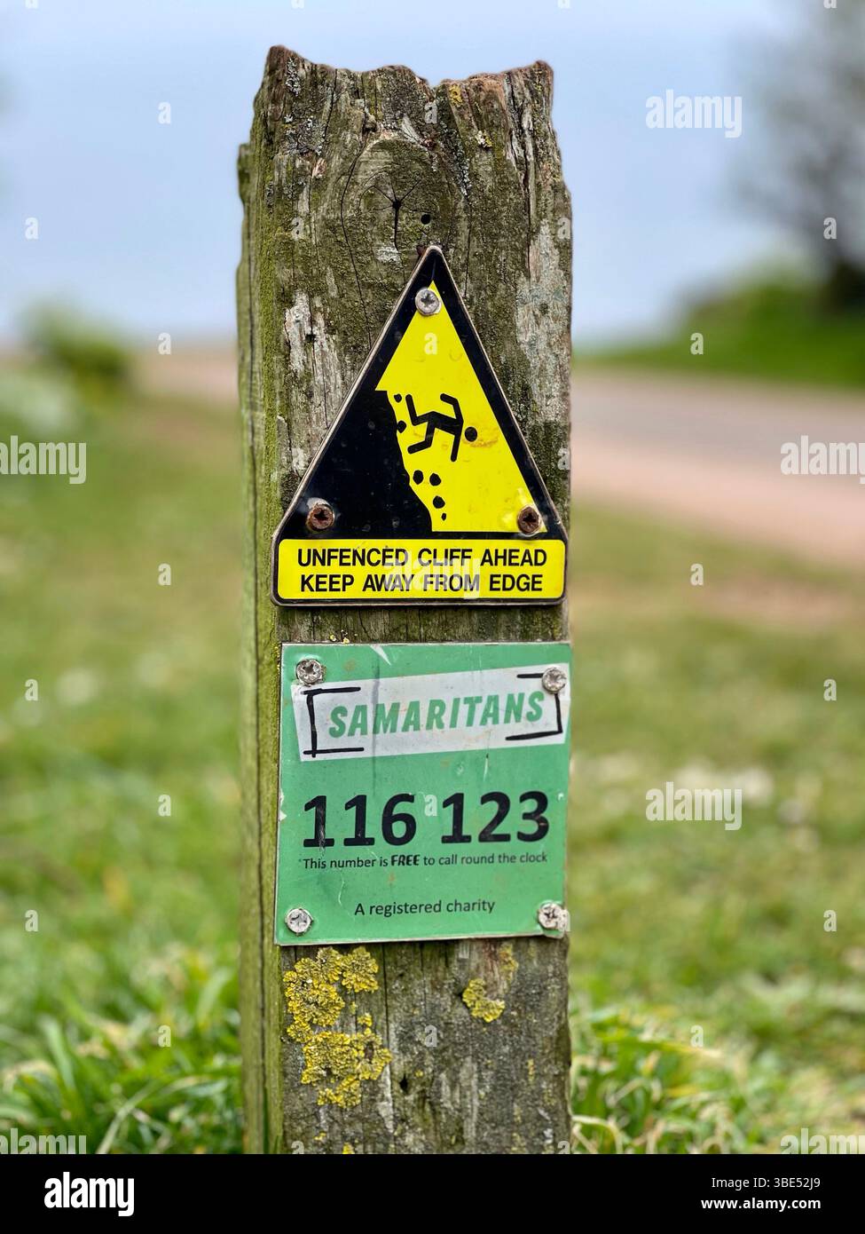Ein Warnschild in der Nähe einer steilen Klippe, das zur Vorsicht auffordert und über eine Samaritaner-Hotline Unterstützung für Menschen in Not bietet Stockfoto