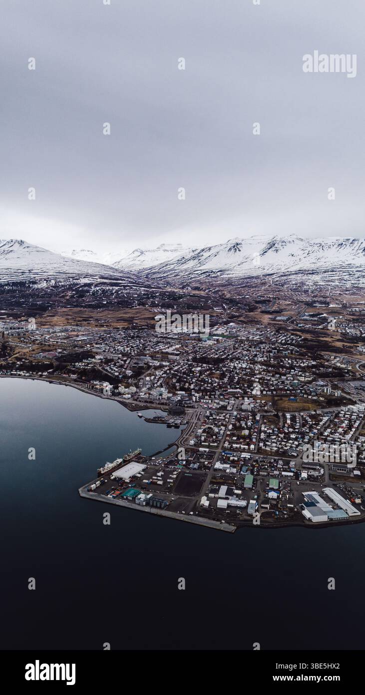 Drohnenblick auf Hofsos, ein kleines Küstendorf im Norden Islands, mit Hafen, Häusern und schneebedeckten Bergen im Hintergrund unter einem Ov Stockfoto
