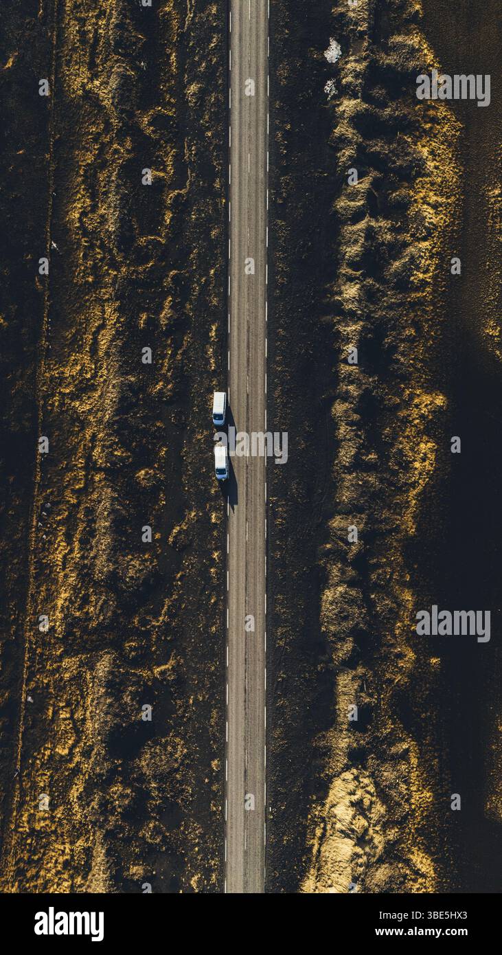 Eine direkte Luftaufnahme von zwei Autos, die auf einer geraden Landstraße fahren, umgeben von goldbraunem Gelände in der Nähe von Hofsos, Island, die auf einem C erfasst wurde Stockfoto