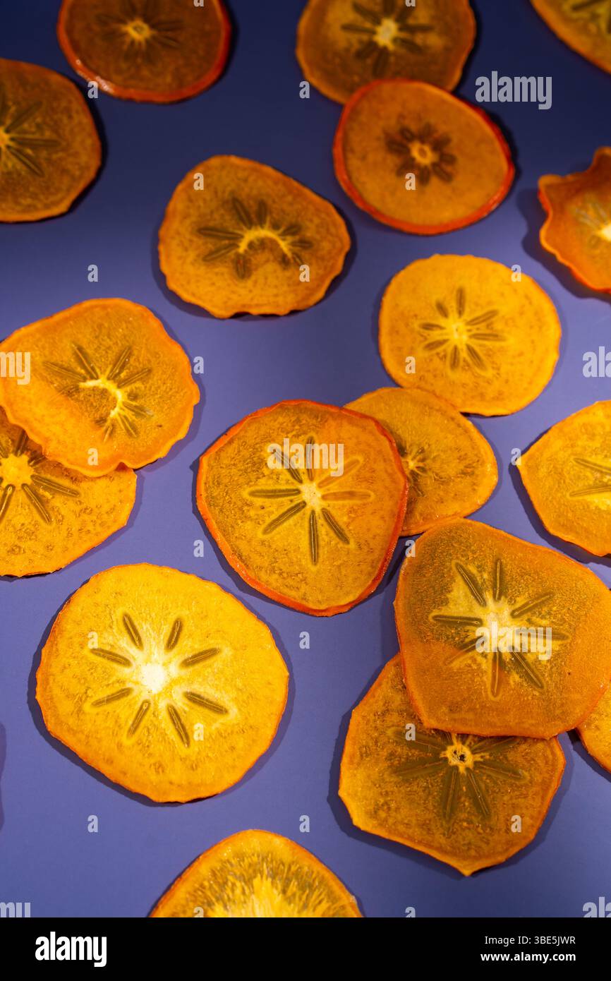 Hell beleuchtete, durchscheinende Scheiben getrockneter Persimmon, die künstlerisch auf einem lebhaften violetten Hintergrund angeordnet sind und ihre einzigartigen sternähnlichen Muster zeigen. Stockfoto