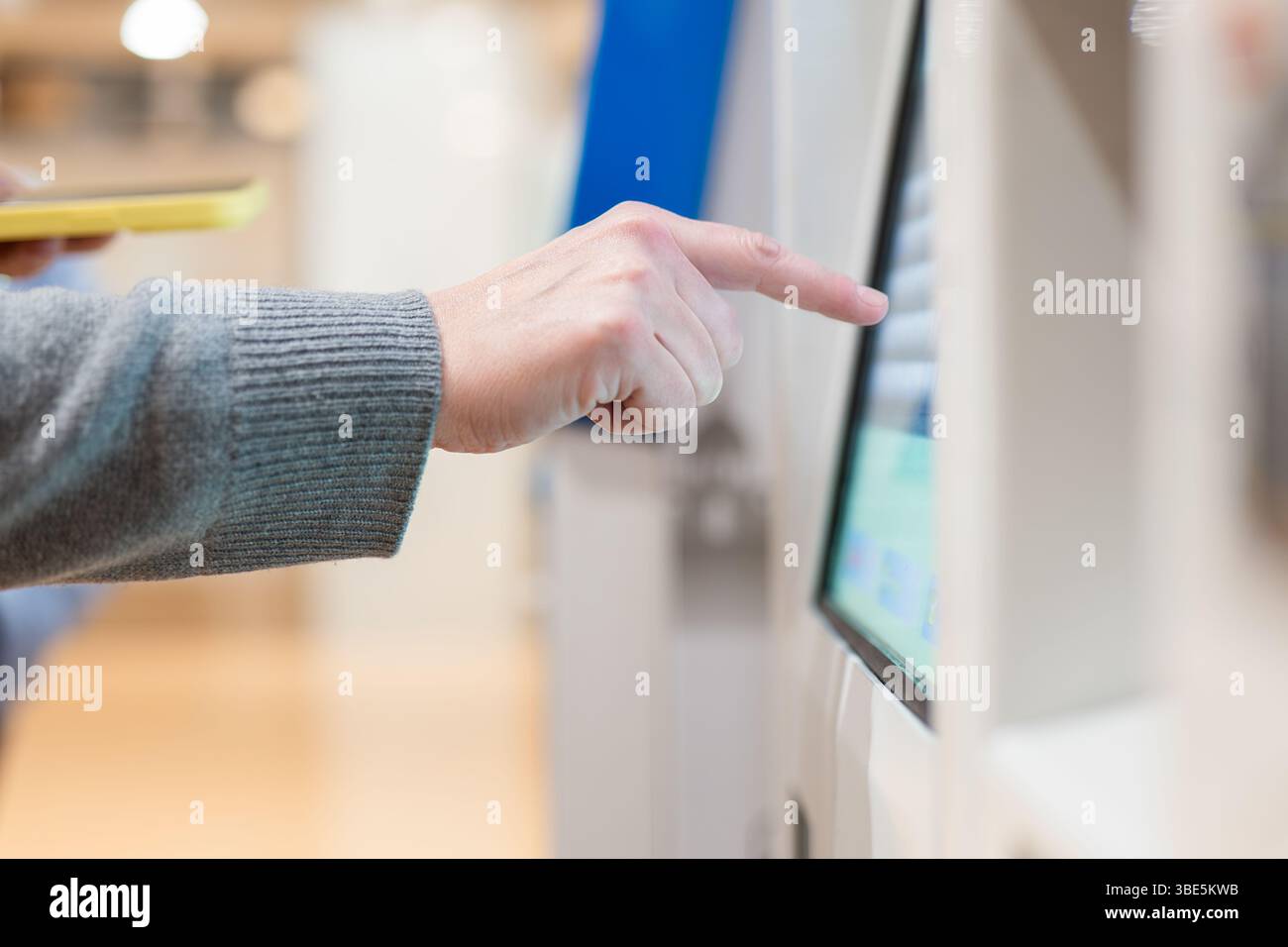 Nahaufnahme der Hand einer Person, die mit einem Touchscreen-Kiosk an einem Flughafen interagiert. Das Bild betont moderne Technologie und Komfort für Trav Stockfoto