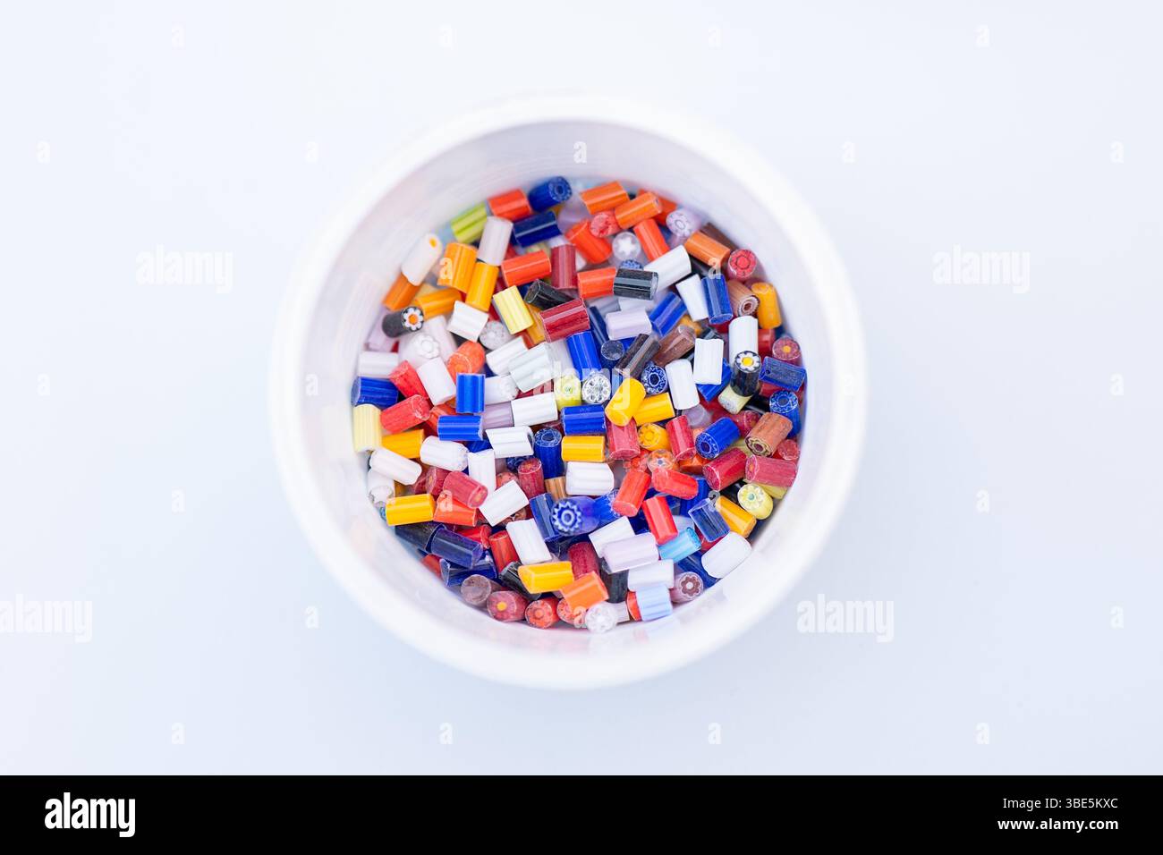 Eine lebendige Ausstellung von bunten Muranoglasstücken füllt eine weiße Schüssel. Dieses atemberaubende Beispiel venezianischer Handwerkskunst zeigt die Schönheit der Mura Stockfoto