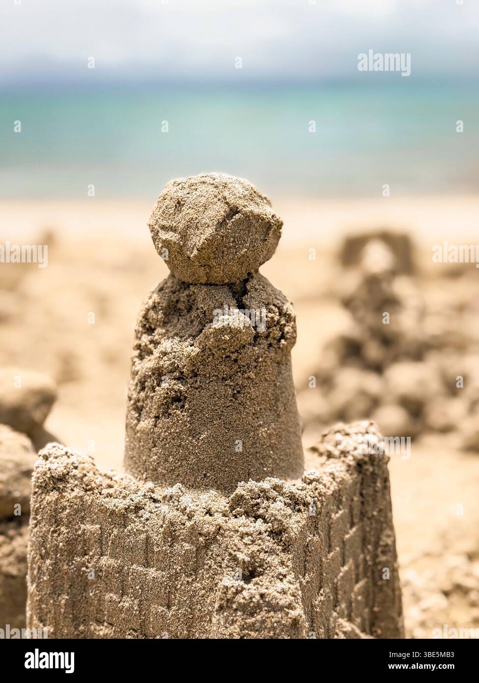 Eine detaillierte Sandburg steht stolz am Meer, mit komplizierten Designs und einer glatten Kuppel vor einem Hintergrund von klarem blauem Himmel und fernen Oce Stockfoto
