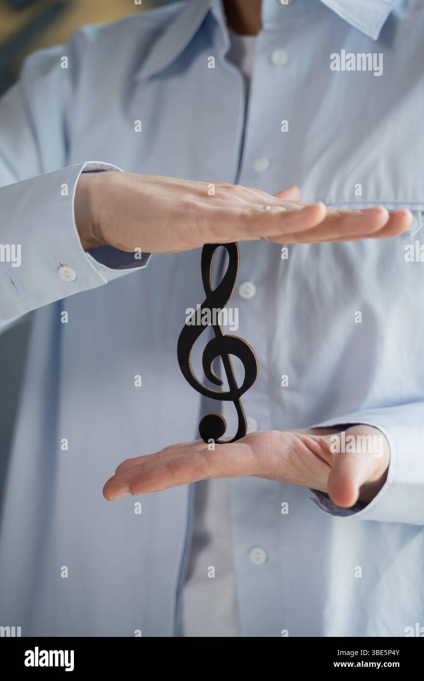 Eine Person, die ein hellblaues Hemd trägt, benutzt beide Hände, um ein Symbol für einen hohen Schlüssel zu halten. Das Bild symbolisiert die Harmonie und Balance, die in Musik und zu finden sind Stockfoto