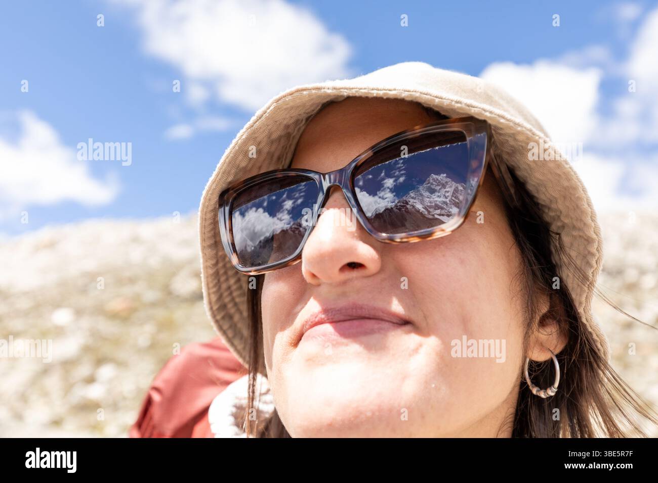 Nahaufnahme einer lächelnden Frau mit Sonnenbrille und Hut, die den majestätischen Blick auf den Mount Everest widerspiegelt. Der klare Himmel trägt zum adve-Gefühl bei Stockfoto