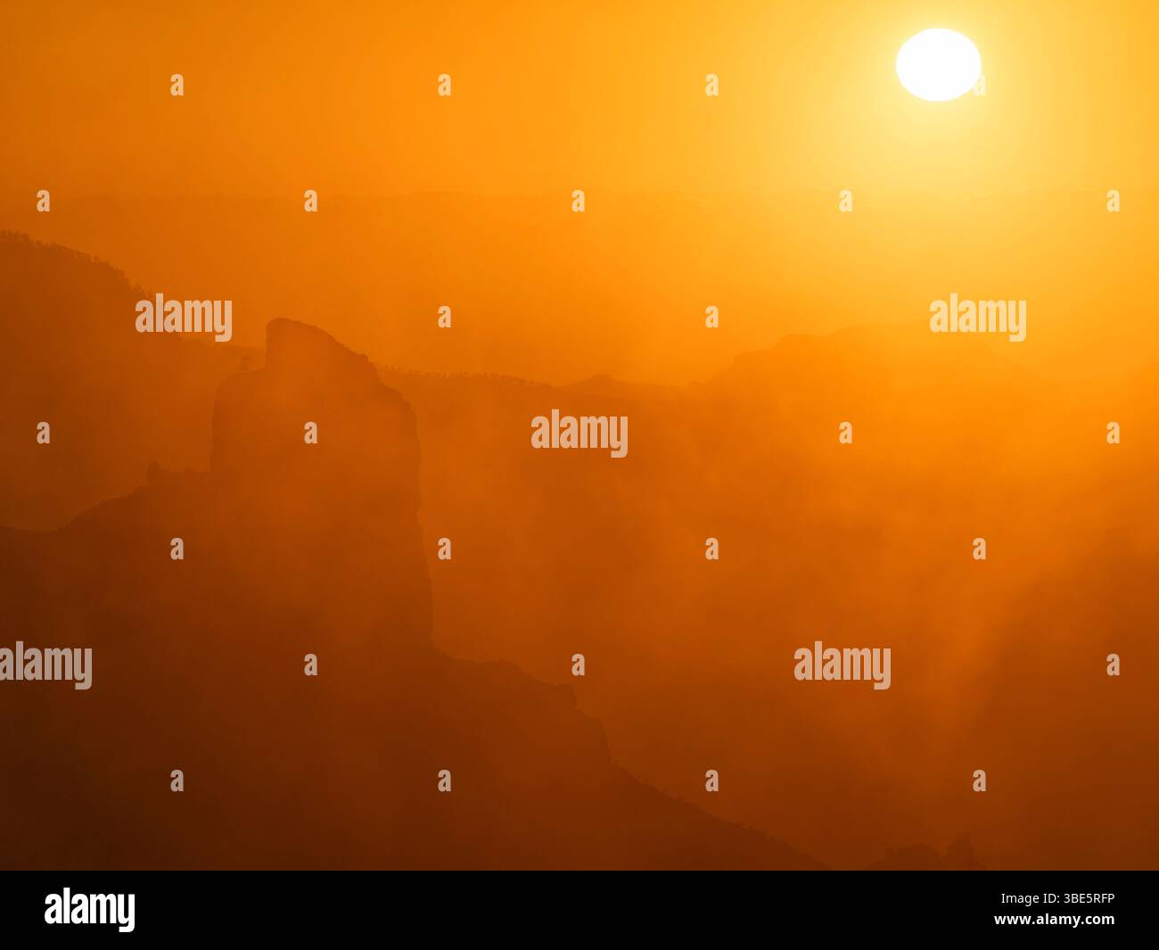 Ein faszinierender Blick auf den Roque Nublo unter einem goldenen Sonnenaufgang, mit Silhouetten von Bergen, die von einem nebeligen, ätherischen Leuchten auf Gran Canaria umgeben sind. Stockfoto