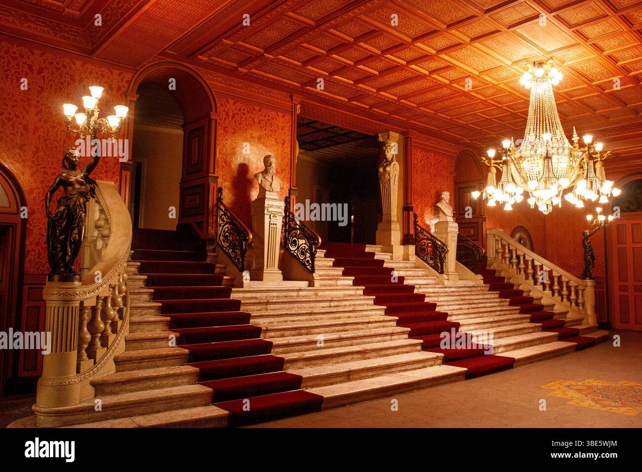 Die große Marmortreppe des Theatro da Paz in Belém, Pará, beleuchtet von einem verzierten zentralen Kronleuchter und flankiert von bronzenen Fackelstatuen. Stockfoto