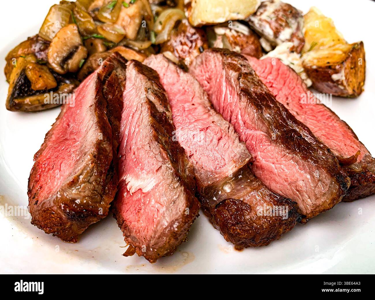 In Scheiben geschnittenes mittelseltenes Steak mit Pilzen und gerösteten Kartoffeln. Stockfoto