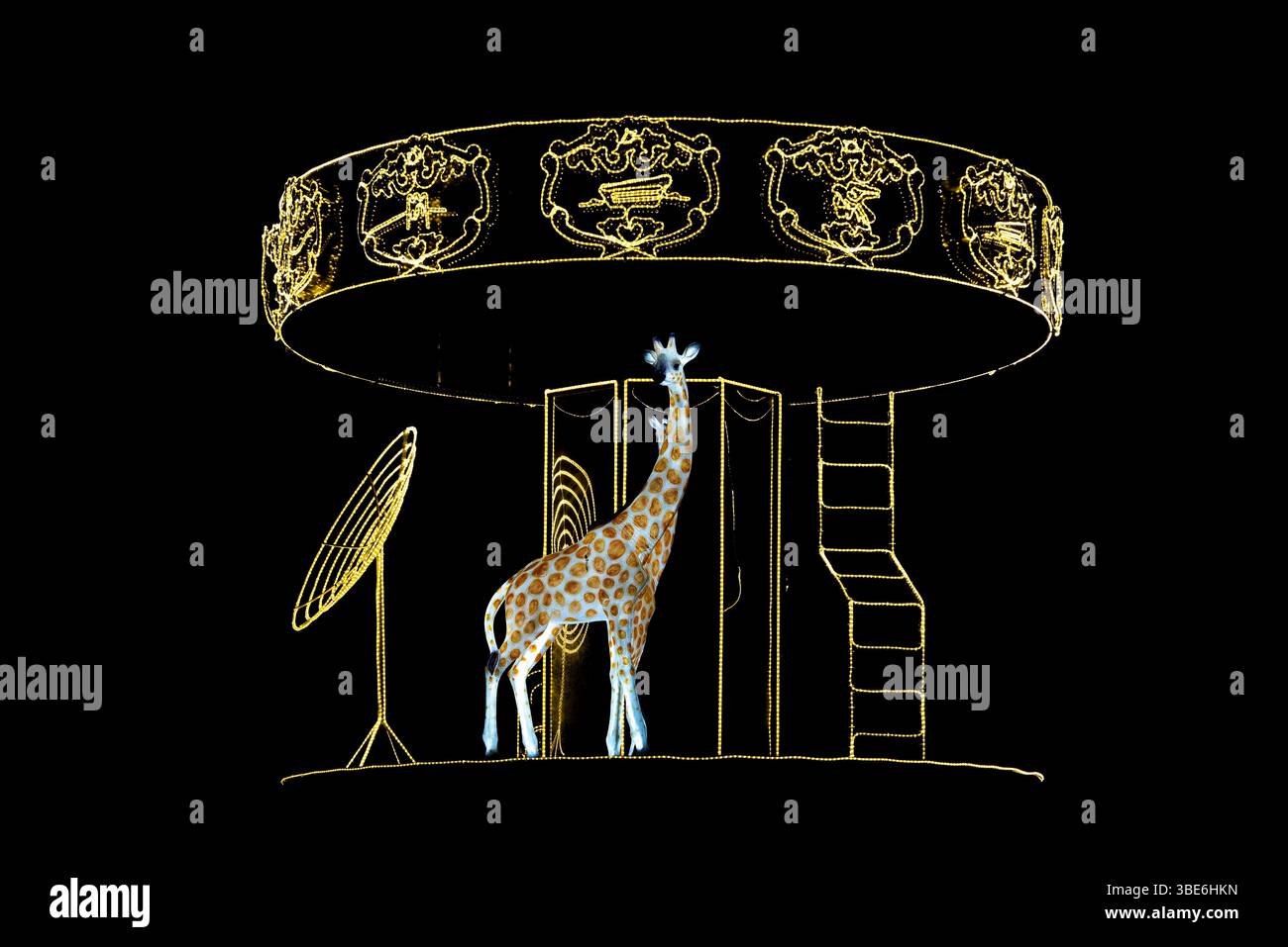 Eine leuchtende Giraffe steht unter dem beleuchteten Karussell mit goldenen Tiermotiven in der Eastern Mangrove in Abu Dhabi, Vereinigte Arabische Emirate, die nachts leuchtet. Stockfoto