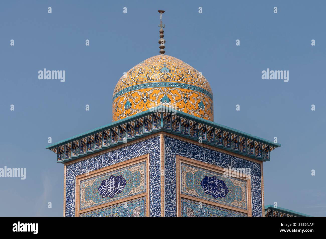 Die herrliche goldene Kuppel mit blauen islamischen Kalligraphiebändern krönt die traditionelle Moschee-Architektur unter dem hellblauen Himmel in A'ali. Stockfoto